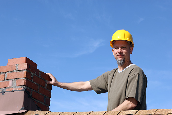 Man in hardhat on roof inspecting chimney 